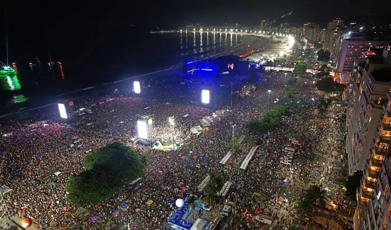 Multidão reunida na praia de Copacabana durante show noturno, com luzes e emoção coletiva representando a força da cultura latina.